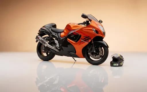 Suzuki Hayabusa orange et noire, moto sportive vue de trois quarts avant en studio sur fond beige, casque posé au sol